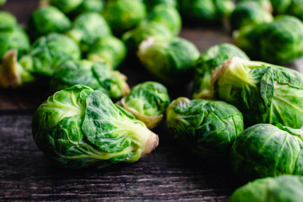 vista de cerca de coles de bruselas frescas esparcidas en una mesa de madera oscura - brussels sprout raw brown close up fotografías e imágenes de stock