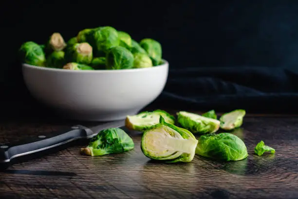 Halving fresh Brussels sprouts on a dark wood background
