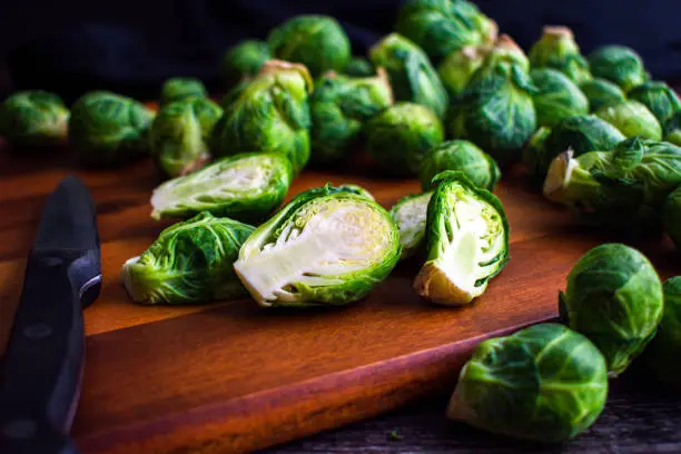 Fresh brussels sprouts halved with a paring knife on a wooden carving board