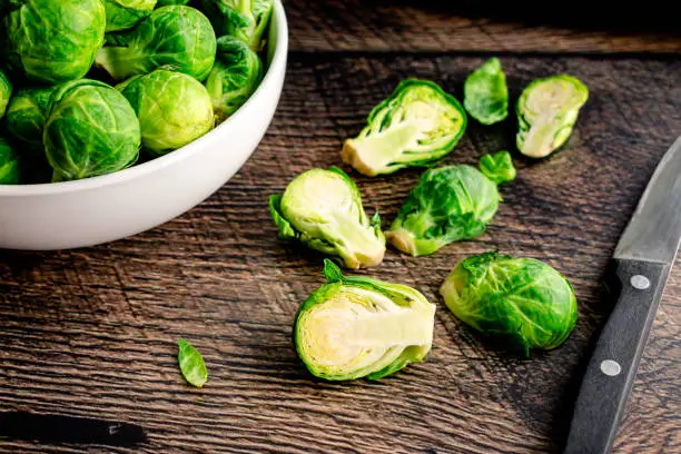 Halving fresh Brussels sprouts on a dark wood background