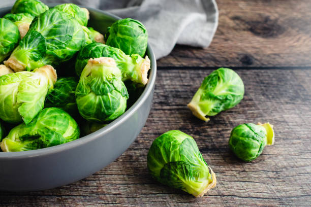 vista de cerca de coles de bruselas frescas esparcidas en una mesa de madera oscura - brussels sprout raw brown close up fotografías e imágenes de stock