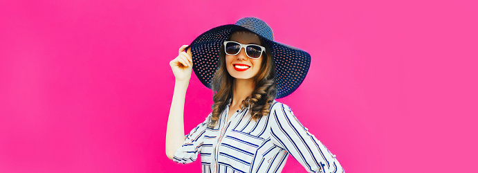 Portrait of beautiful smiling woman model wearing summer straw hat, white striped shirt on pink background
