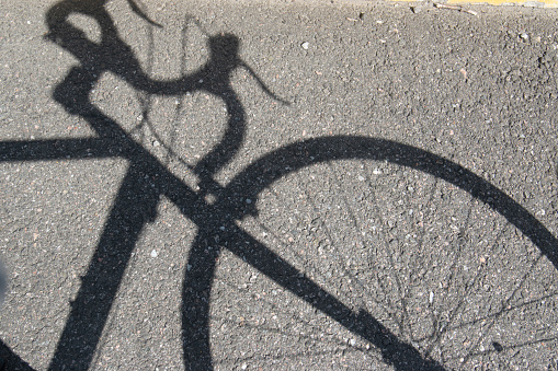 The shadow of a road bike is seen on the asphalt. The shadow of the front wheel,  handle bars and part of the frame is visible. No people are seen in the photo.