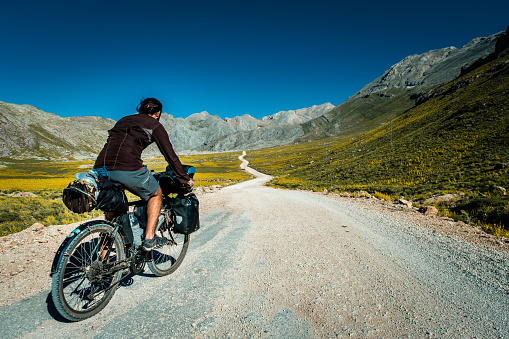 He is 30 years old, doing a camping bike tour. There are various bags on his bike, around 60 liters in total.High altitude. Tour cyclist driving on dirt road in mountainous region. Long and narrow road with curves. Mediterranean region Taurus mountains Antalya.background shot