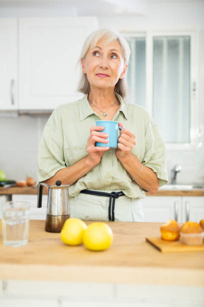 istock Positive old woman drinking coffee in kitchen at home 1412271776