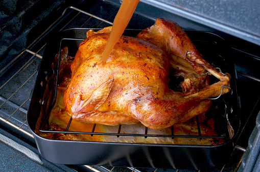Basting a Thanksgiving Turkey in a roasting pan in an oven.