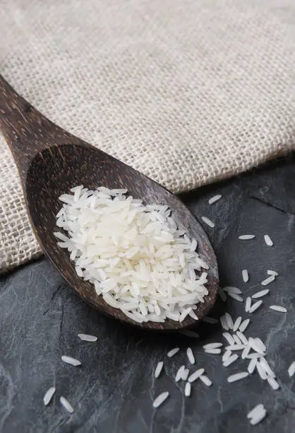 Closeup of a wood spoon with white Jasmine rice, on a slate background and burlap sack.