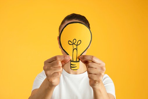 Woman holding light bulb on head against yellow background.
