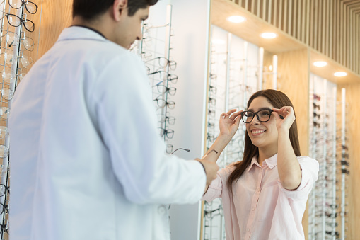 A happy young latin woman trying on eyeglasses with an ophthalmologist at an optical center.