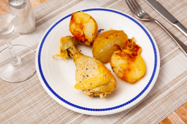 Just cooked chicken leg with fried potatoes served on plate. Poltry dish on table.