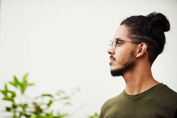 Confident young man with a beard wearing glasses looking sideways while standing outside on a patio at home