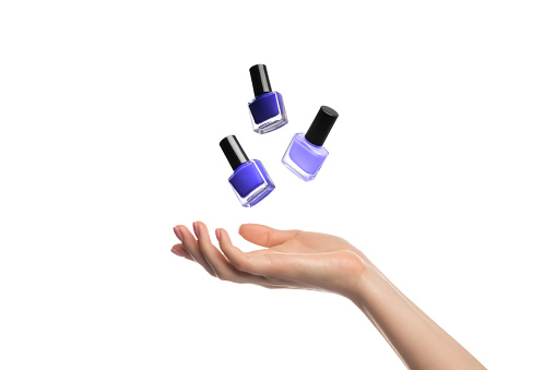 Three shades of violet nail polish bottles levitate, hang over a woman's hand, isolated on white.