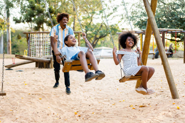 ojciec z córką i synem bawiący się na huśtawce - child swinging playground african descent zdjęcia i obrazy z banku zdjęć