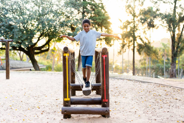 A charming wooden walkway leads visitors to a captivating playground with a prominent grand tree at its center, fostering a serene environment for people of all ages to socialize and play