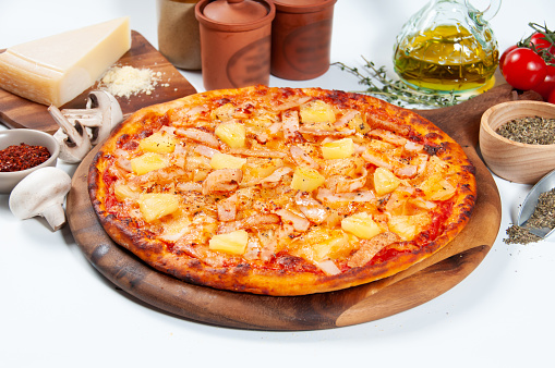Hawaiian Pizza with tomato, onion, chili powder, and black pepper isolated on wooden cutting board side view of fastfood on wooden table
