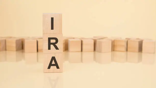 Photo of ira - acronym from wooden blocks with letters, Individual Retirement Account concept on yellow background. copy space available