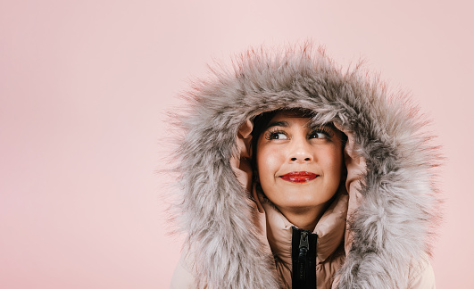 Portrait of young hispanic girl in winter coat smiling looking at camera on pink coral studio background in Mexico Latin America