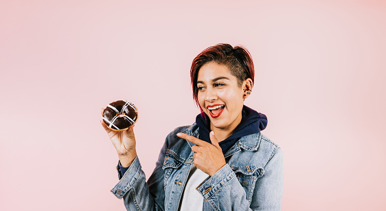 Portrait of young hispanic woman eating donuts on coral pink background in Mexico Latin America