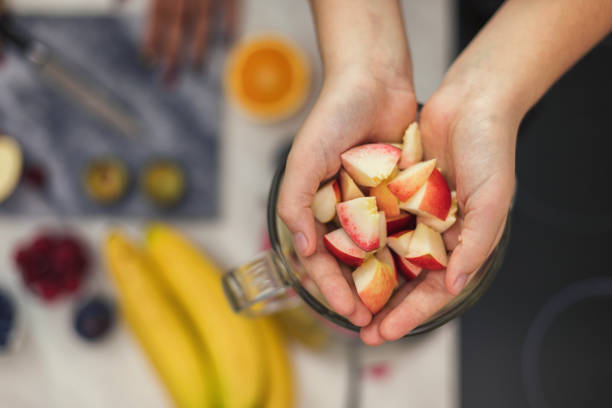 Two teenage girls making fresh organic smoothie using blender in the kitchen