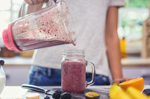 Teenage girl making fresh organic smoothie using blender in the kitchen