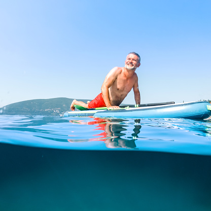 Mature man enjoying on a paddleboard on the beach on a sunny morning.