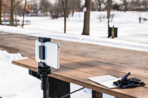 Phone on a tripod, recording video blog on the lake shore on a beautiful cool winter day in the park. Podcast outdoor concept. copy space