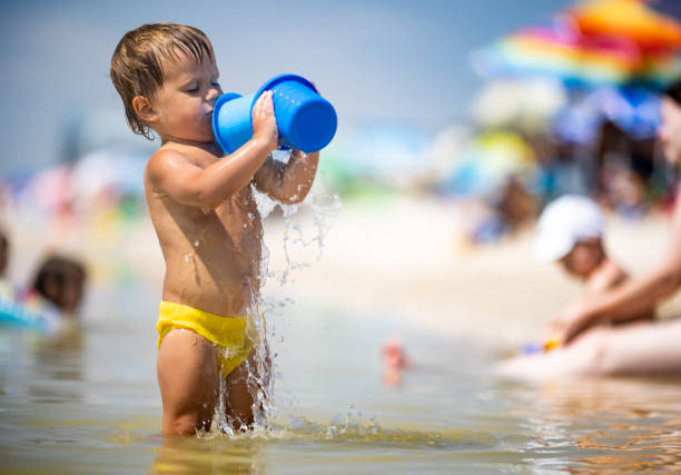 Little funny funny kid, collects shells and pebbles in the calm blue sea on a sandy bottom under the hot summer sun on a bright vacation