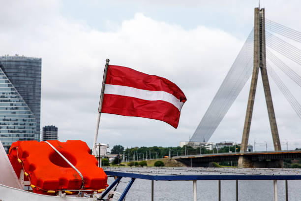 bandeira da república da letônia. ponte de cabo em riga no fundo. - letónia - fotografias e filmes do acervo