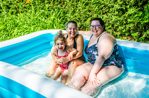 Grandmother, aunt and baby girl playing in toy pool during summer day in Quebec city, Canada.