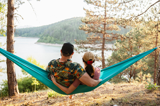 Rear view of couple embracing while sitting in hammock on camping in nature.