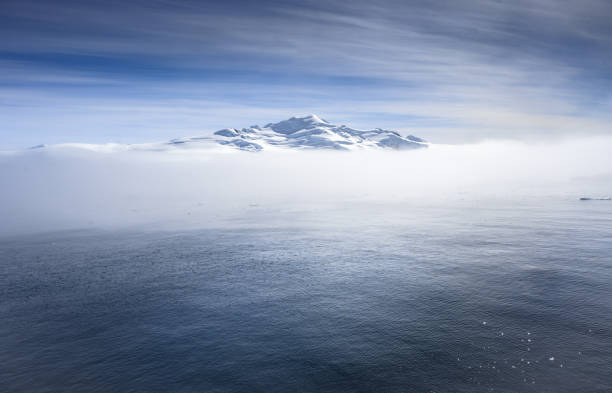 Glacier carpeted mountain and blue sea in the Antarctic Peninsula separated by a cloud bank. Beautiful deep, clear blue.