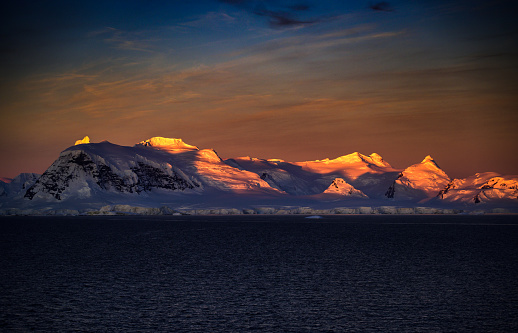 Glistening glacier covered mountains in the last rays of sun. Dramatic shadows along the coast.