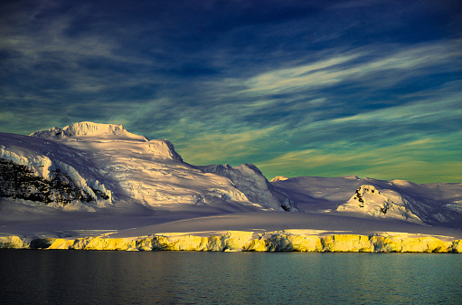 Glacier covered mountain and glacier edge by the sea glistening in the late evening twilight. Antarctic Peninsula.