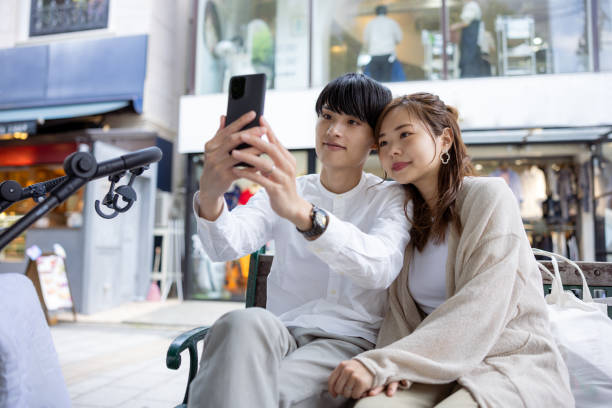 Young family sitting on bench and taking selfie picture in city stock photo