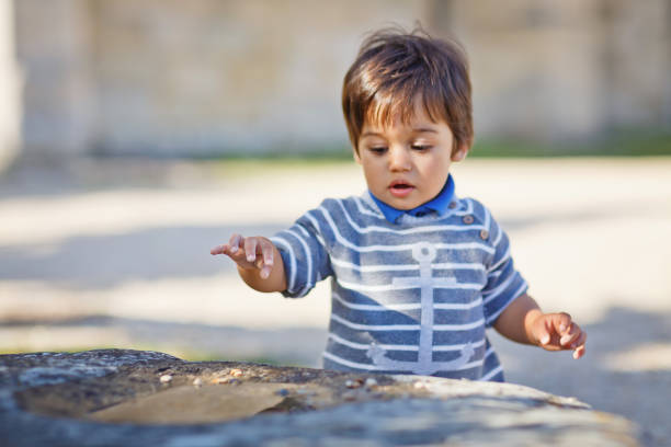portrait d’un petit petit garçon oriental jouant en plein air dans le parc. enfant arabe amusant dans la rue avec des cailloux dans une flaque d’eau - cute boy photos et images de collection