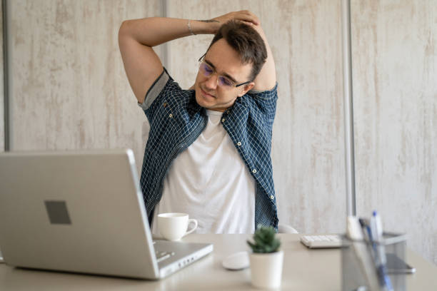 istock young man stretching at work while sitting at desk having back pain 1412346479