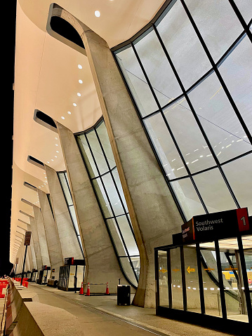 Dulles, Virginia, USA - July 10, 2022: The inside of the nearly empty main terminal at Washington Dulles International Airport (IAD) can be seen through the glass facade between the supports for the catenary curve ceiling of the iconic main terminal at 2am.