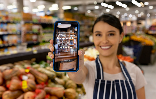 Female Latin American market vendor making a survey about customer experience at a supermarket using a mobile app