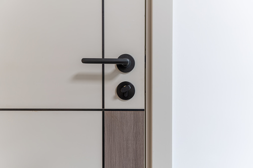 Modern door handle with lock and magnetic latch. White wooden Interior door, close up.