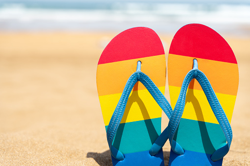 colorful slippers on the beach on a summer day - gay pride flag - flip flops