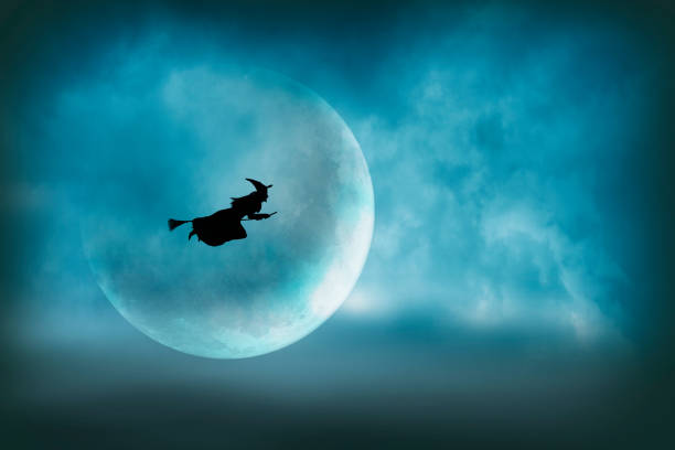 Flying Halloween Witch Silhouetted In Front of Large Moon stock photo