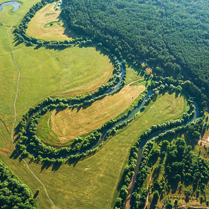 Aerial view of the winding river among the agriculture fields and forest at sunset