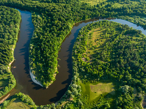Aerial view of the beautiful river turn among the forest and meadows at sunset