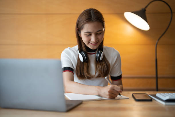 istock Asian woman writing making list taking notes in notepad working or learning on laptop indoors- educational course or training, seminar, education online concept 1412370561