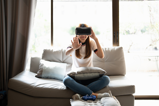 Concept of technology,gaming,entertainment and people.asian woman enjoying virtual reality glasses while relaxing in living room.Happy young guy with VR headset playing video game at home.
