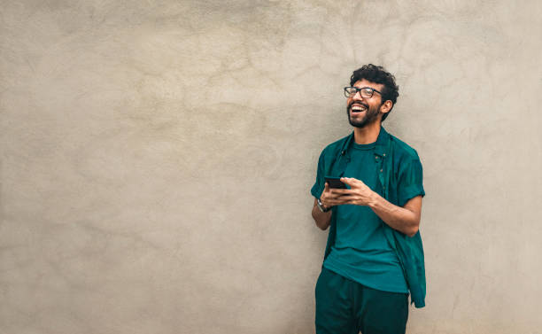 istock Happy latin man with his cell phone leaning against a wall with copy space, Person smiling phone with space for text. Happy handsome guy leaning against the wall using his cell phone 1412374823