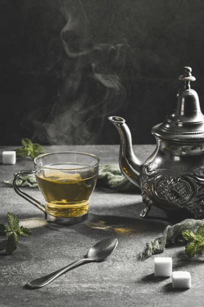 teiera tradizionale marocchina con una tazza fumante di tè in un'atmosfera nera fumosa. formato verticale. - morocco tea glass mint tea foto e immagini stock