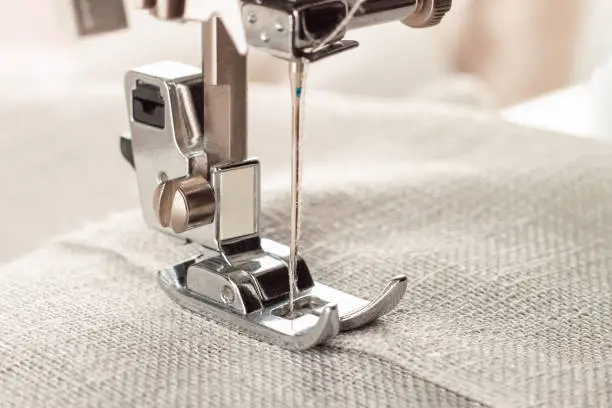 Modern sewing machine presser foot with linen fabric and thread, closeup, copy space. Sewing process clothes, curtains, upholstery. Business, hobby, handmade, zero waste, recycling, repair concept