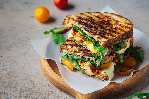 Grilled sandwich with vegetables and mozzarella on a wooden board.