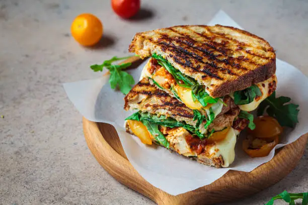 Photo of Grilled sandwich with vegetables and mozzarella on wooden board.